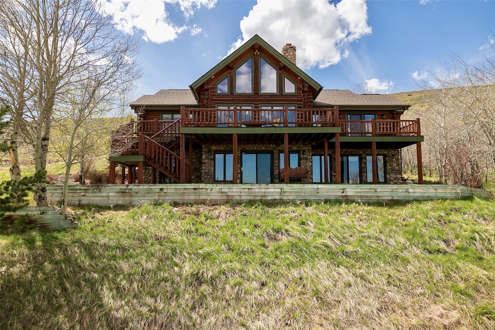 Back of property featuring stone siding, a chimney, a deck, and log exterior