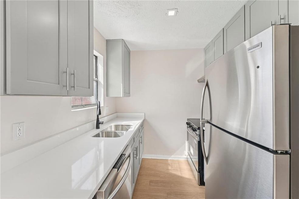 Kitchen featuring gray cabinetry, appliances with stainless steel finishes, light stone countertops, light wood-style flooring, and a textured ceiling