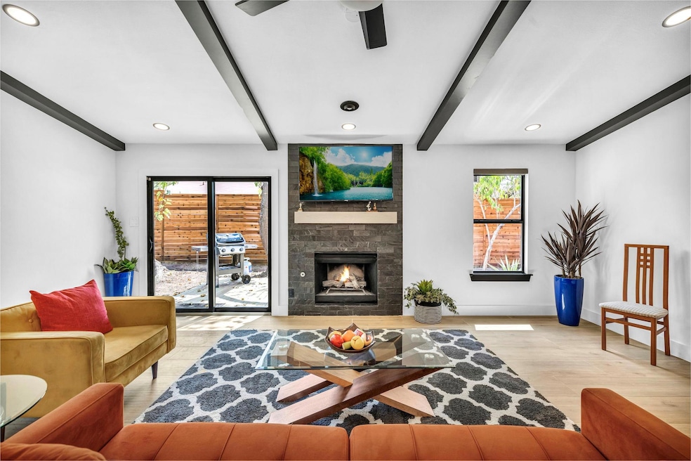 Living area with beamed ceiling, a large fireplace, light wood finished floors, and recessed lighting