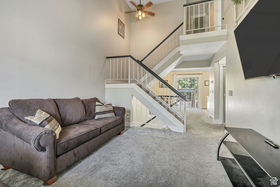 Carpeted living area with a high ceiling, ceiling fan, and stairs