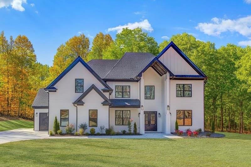 View of front facade with a front yard, board and batten siding, concrete driveway, and a shingled roof