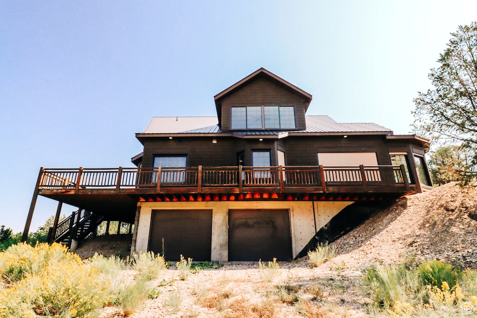 Rear view of house featuring a deck, a metal roof, stairs, dirt driveway, and a garage