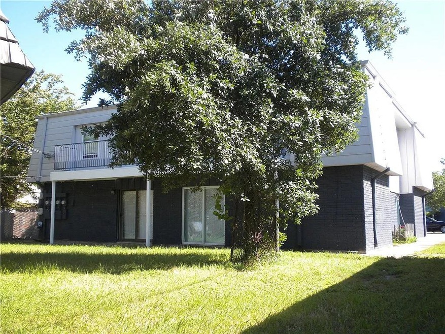 Rear view of property featuring brick siding, a lawn, and a balcony