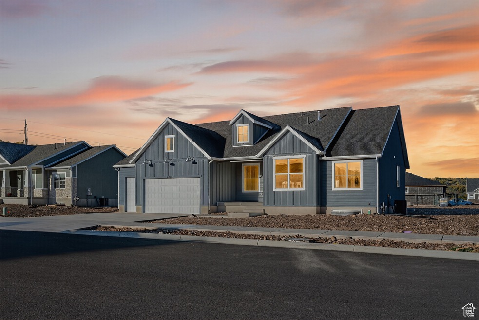 View of front facade featuring board and batten siding, driveway, a garage, and roof with shingles