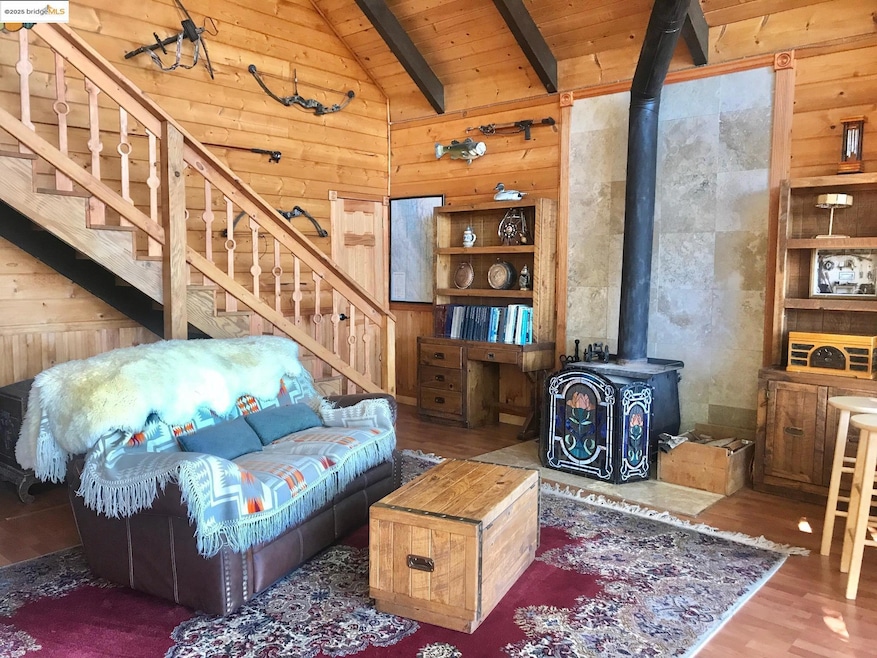 Living room with stairway, wooden walls, a wood stove, wood finished floors, and a wooden ceiling with exposed beams