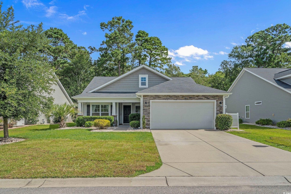 Craftsman-style house with stone siding, an attached garage, a front yard, and concrete driveway