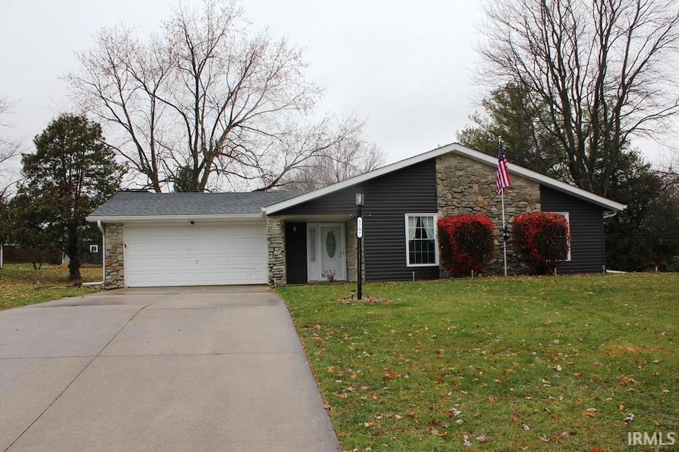 View of front of property featuring stone siding, an attached garage, driveway, and a front yard