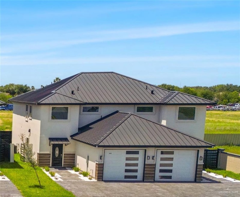 View of front of house with fence, stucco siding, a standing seam roof, driveway, and metal roof
