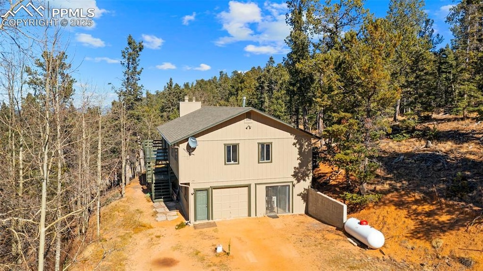 View of side of property with dirt driveway, a chimney, stairs, and a forest view