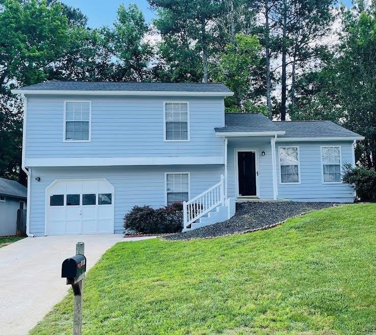 Tri-level home featuring an attached garage, a front yard, and concrete driveway