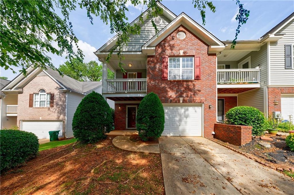 View of front of property featuring brick siding, an attached garage, a balcony, and driveway