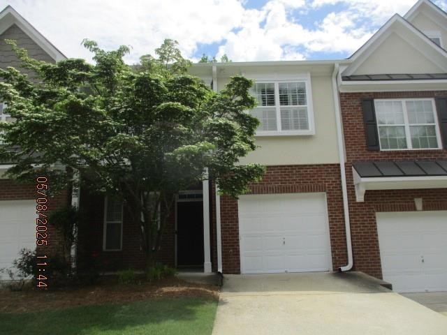 Townhome / multi-family property featuring a standing seam roof, brick siding, an attached garage, concrete driveway, and stucco siding