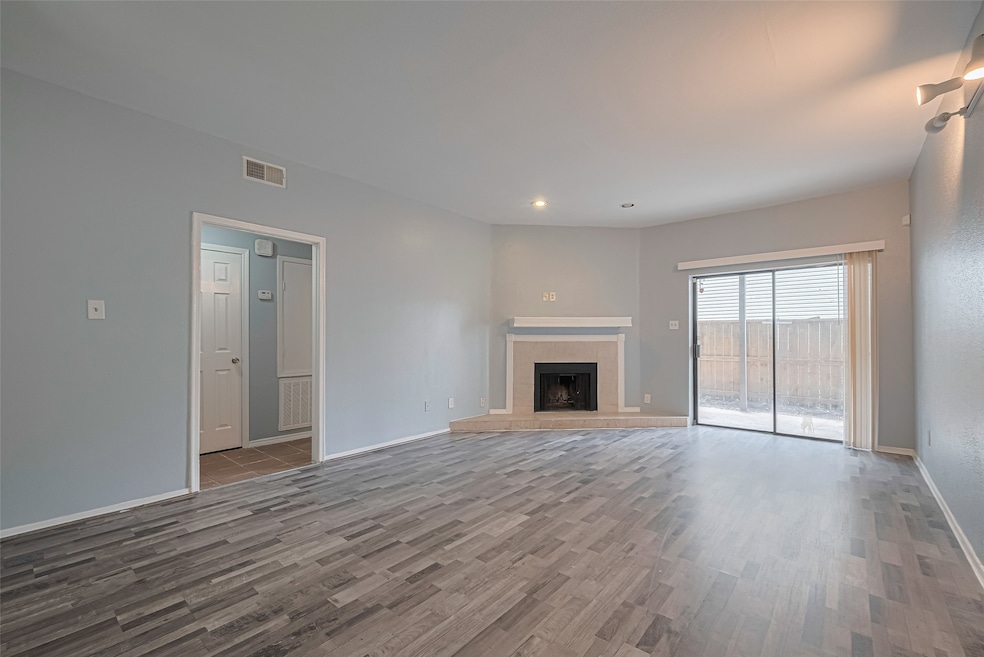 The spacious living area welcomes you with soft natural light pouring through sliding glass doors that lead outside. A fireplace anchors the room, while recessed and track lighting enhance the cozy ambiance. An open layout seamlessly connects this space to the adjacent dining area.