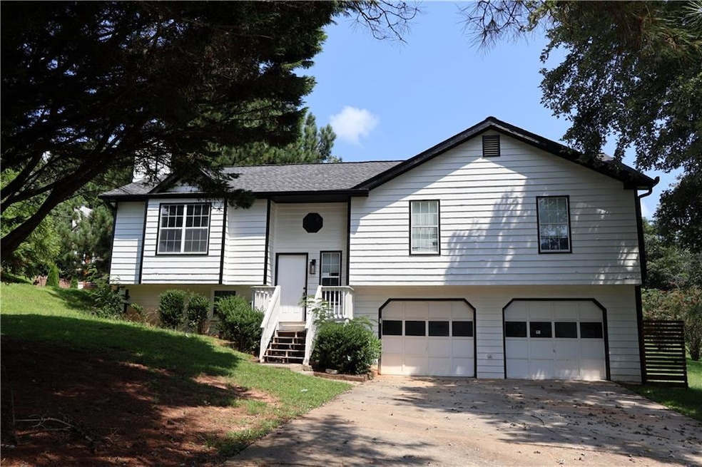 Bi-level home featuring a garage, driveway, a shingled roof, and a front yard