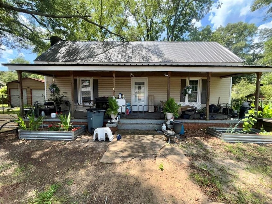 Farmhouse inspired home featuring covered porch, a metal roof, and a vegetable garden