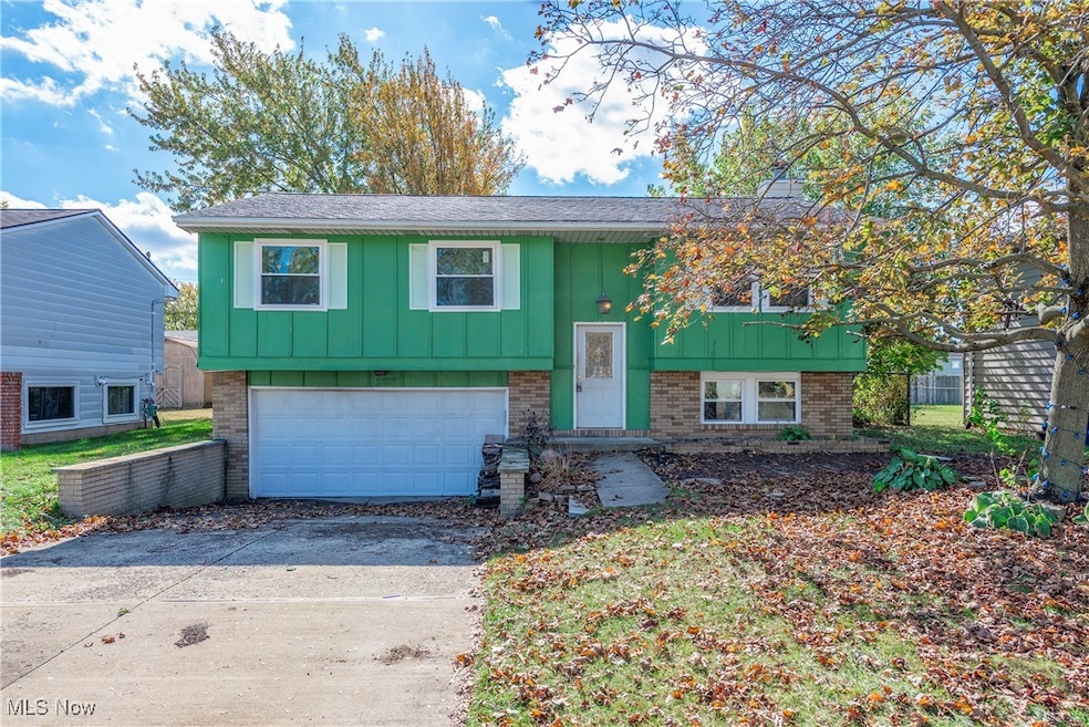 Split foyer home featuring brick siding, driveway, a garage, board and batten siding, and roof with shingles