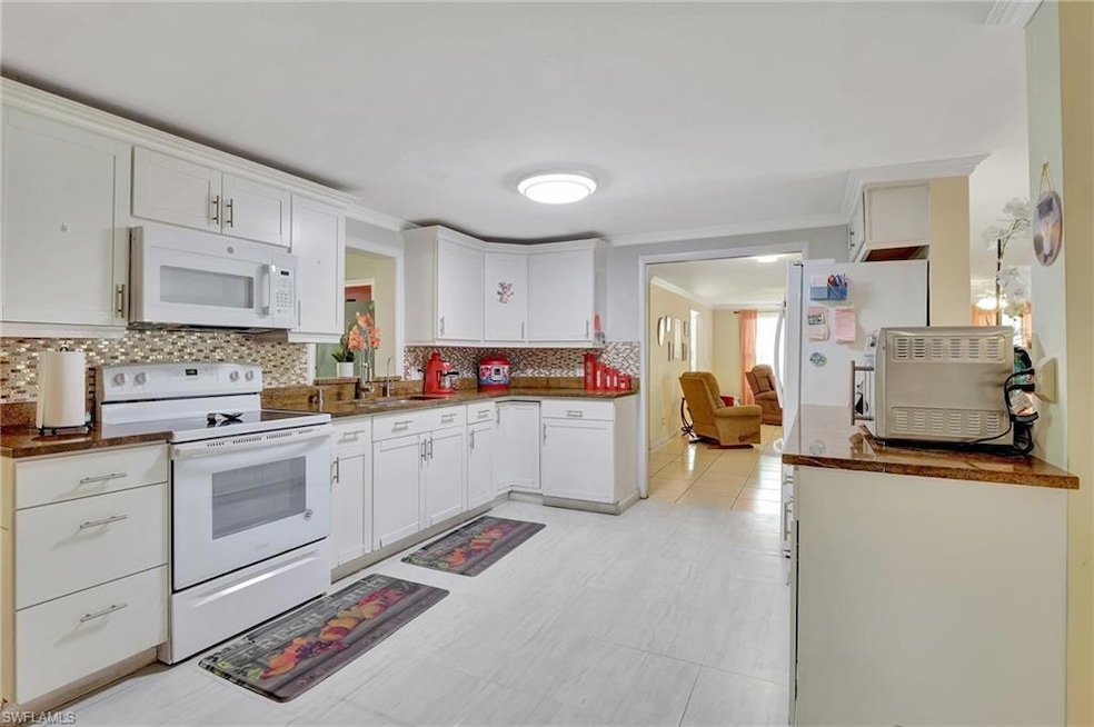 Kitchen with white appliances, backsplash, dark countertops, white cabinets, and crown molding