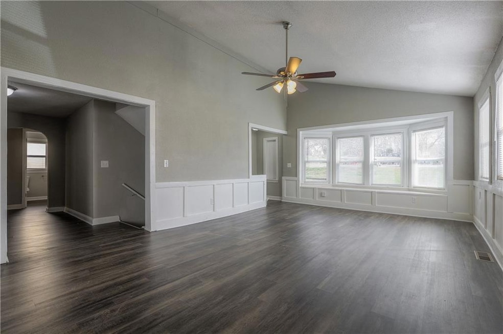 Spare room featuring arched walkways, ceiling fan, lofted ceiling, dark wood-style flooring, and a wainscoted wall