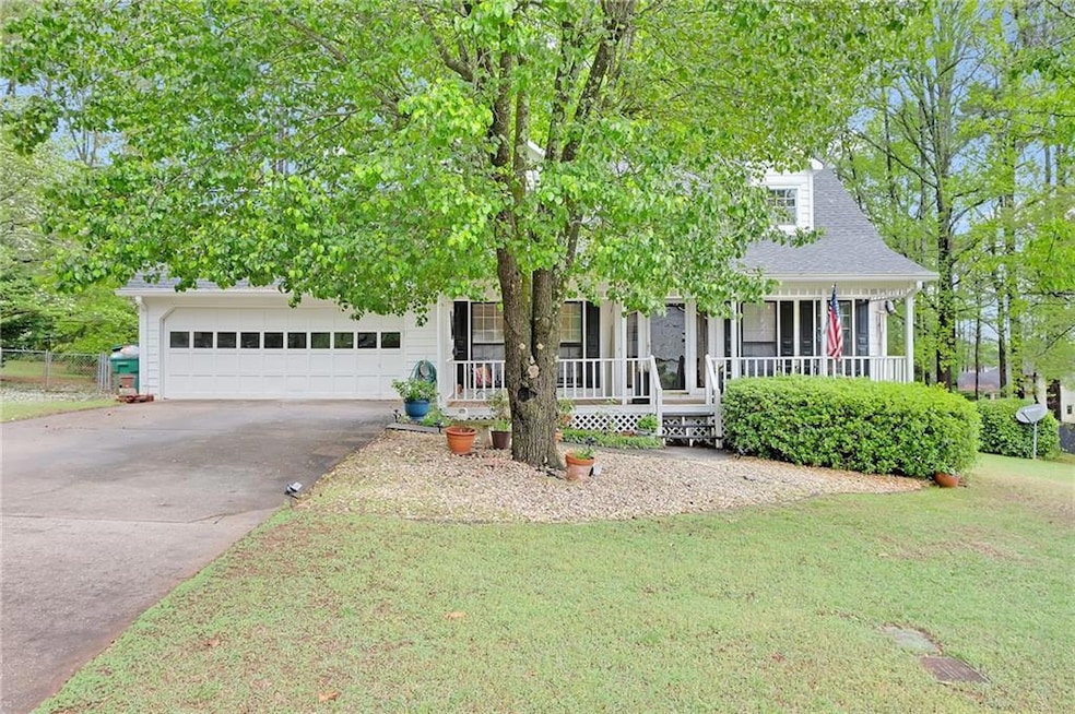 View of property hidden behind natural elements featuring covered porch, a garage, driveway, a front yard, and a shingled roof