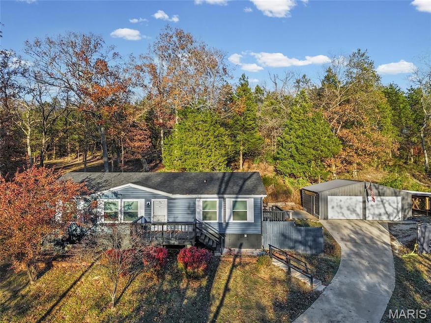 View of front of house with an outdoor structure, a garage, a deck, driveway, and a view of trees