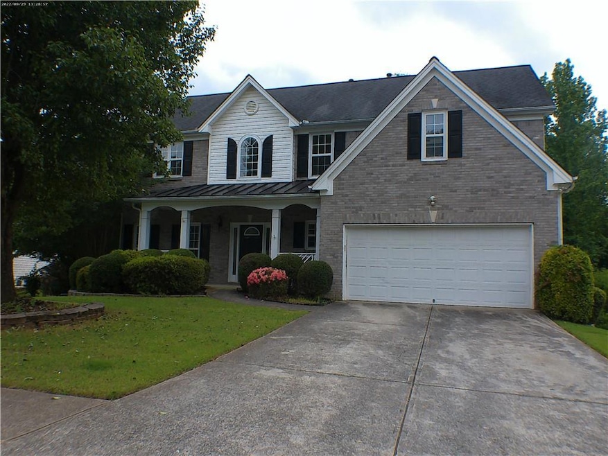 View of front of house with concrete driveway, a standing seam roof, a front yard, brick siding, and covered porch
