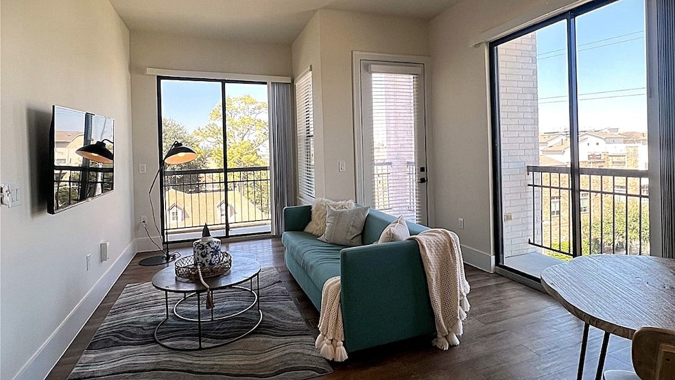 This bright and modern living room features large windows and a sliding glass door, offering plenty of natural light and views. A cozy seating area inviting space with light-color walls and wood flooring.