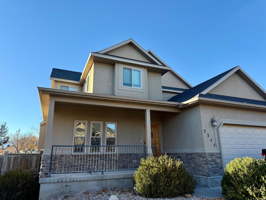 View of front facade featuring stucco siding, stone siding, covered porch, and an attached garage