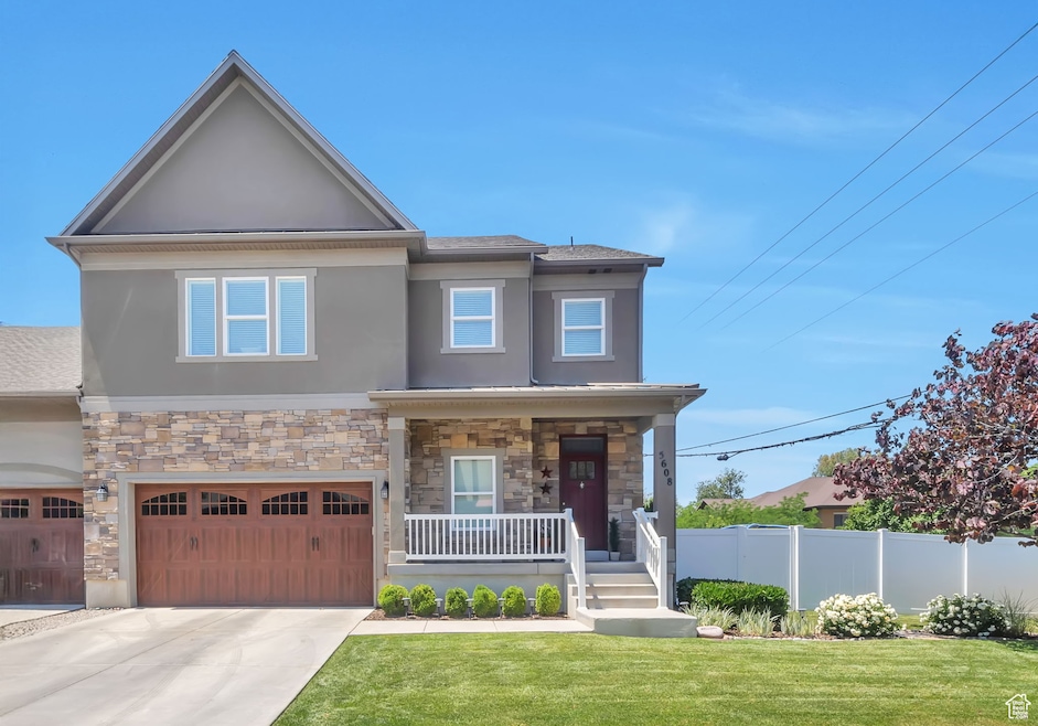 View of front of property with stucco siding, a porch, stone siding, and driveway