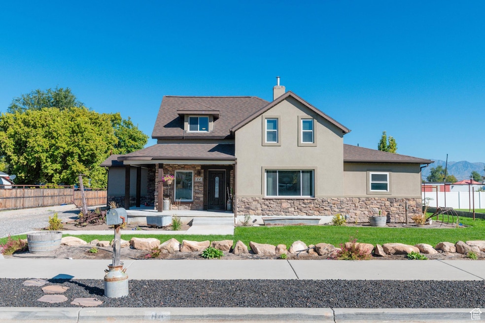 View of front of property featuring covered porch, stone siding, stucco siding, roof with shingles, and a chimney
