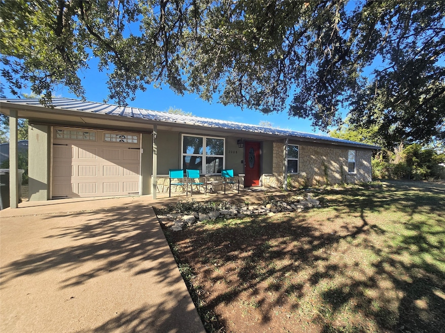Ranch-style house featuring an attached garage, a metal roof, concrete driveway, a front yard, and a porch
