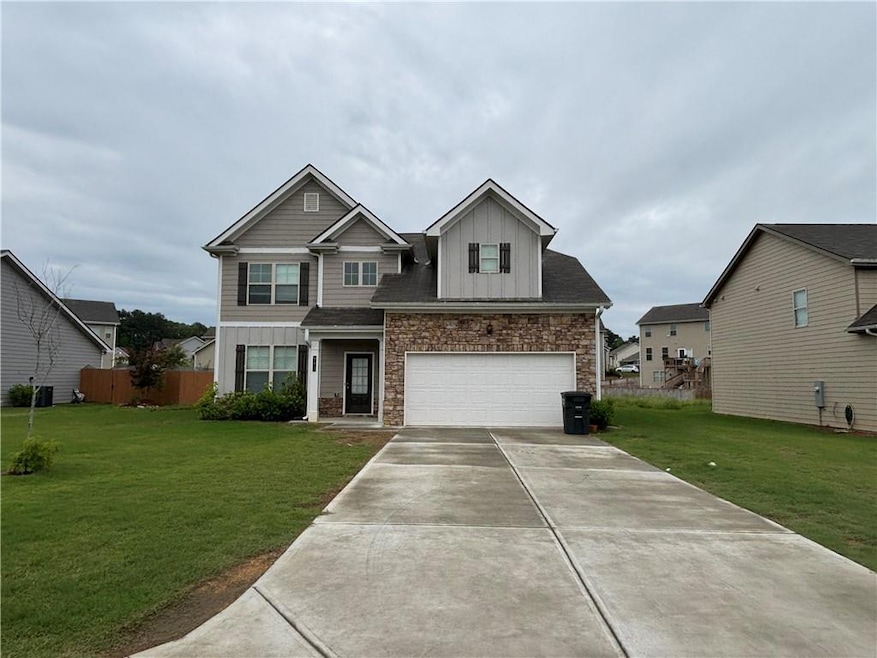 View of front facade featuring board and batten siding, a garage, driveway, a front lawn, and stone siding
