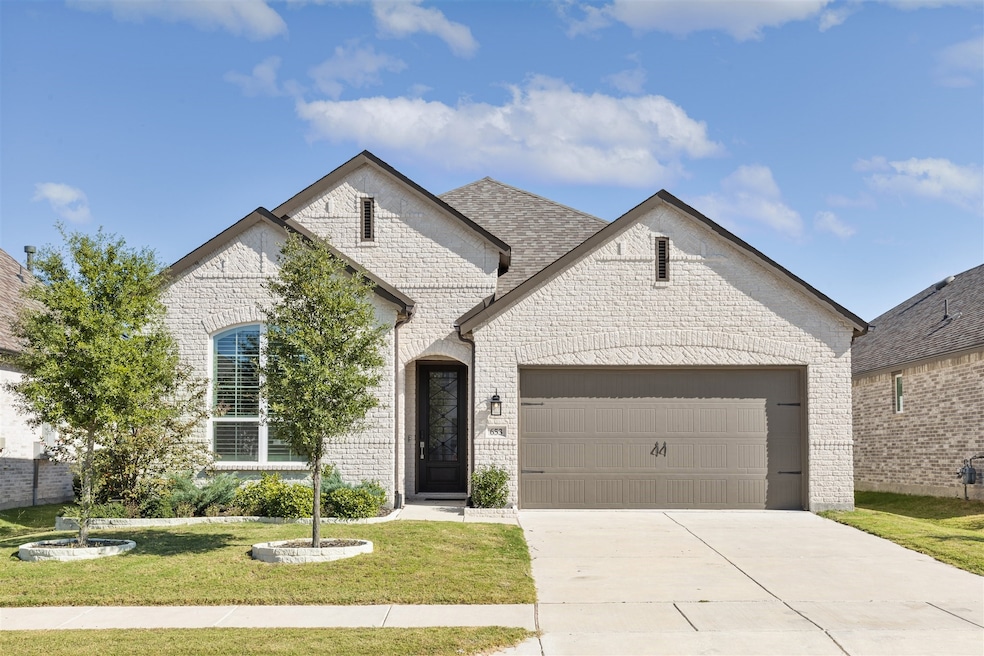 French country inspired facade featuring brick siding, a front yard, a garage, and driveway