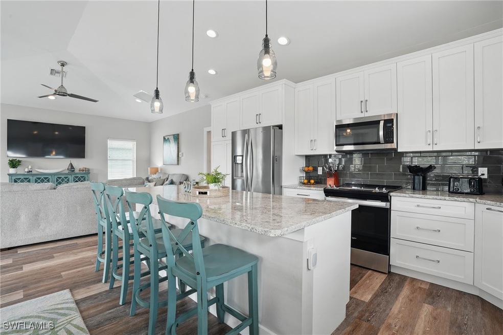 Kitchen with appliances with stainless steel finishes, open floor plan, ceiling fan, tasteful backsplash, and dark wood-type flooring