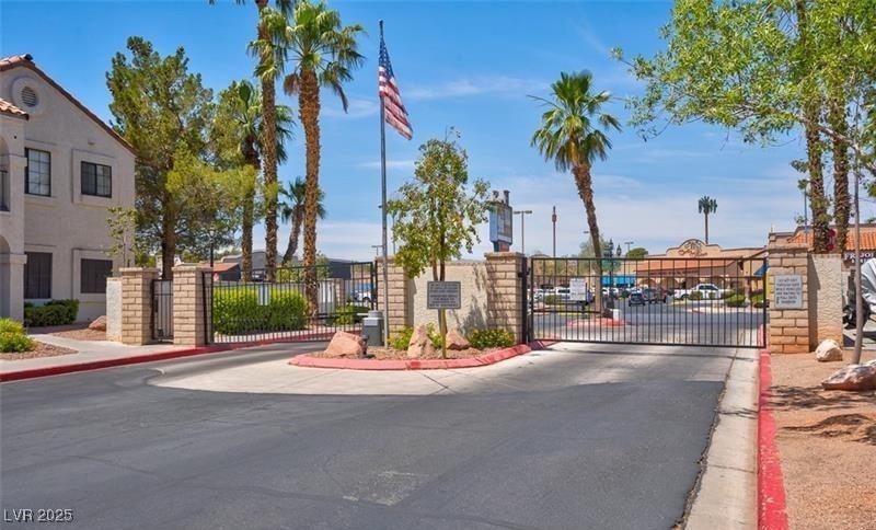 View of asphalt road featuring a gate, curbs, a gated entry, and sidewalks