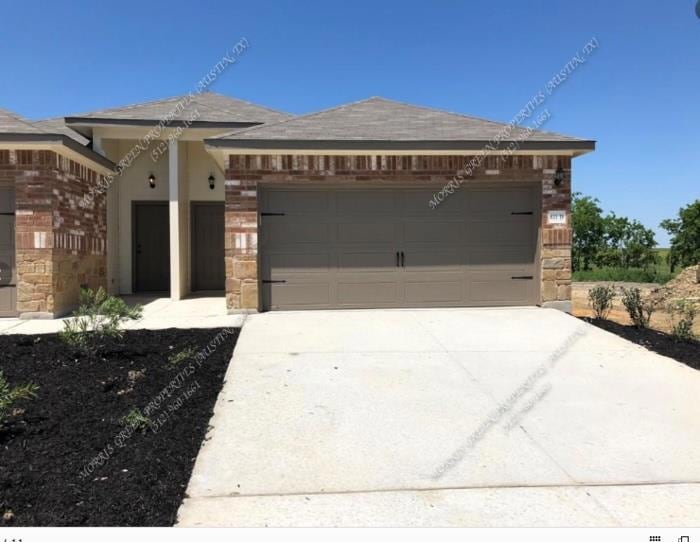 View of front of home featuring stone siding, driveway, an attached garage, and brick siding