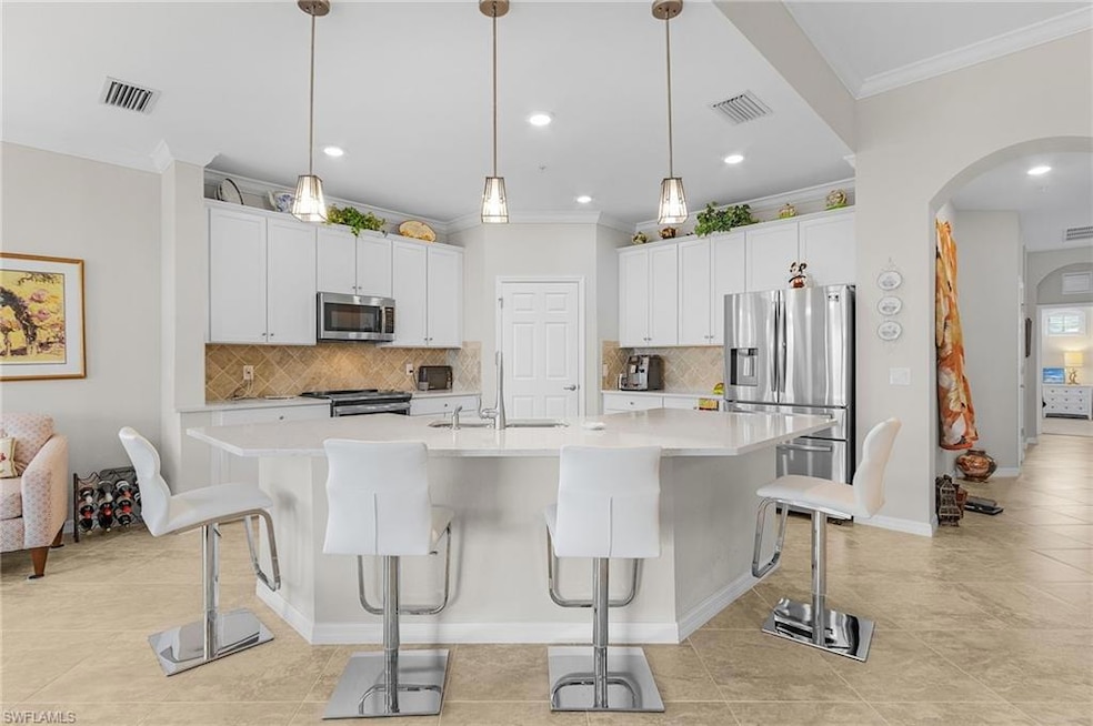 Kitchen featuring appliances with stainless steel finishes, a sink, crown molding, arched walkways, and tasteful backsplash