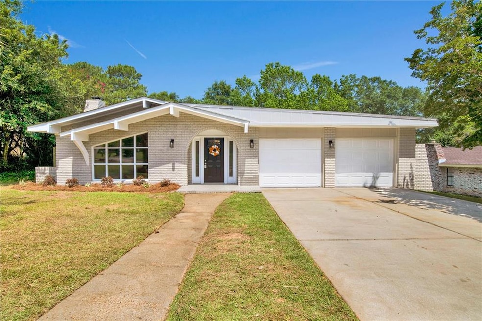 Mid-century inspired home with brick siding, a garage, driveway, and a chimney