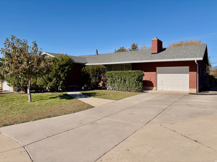 Single story home featuring a front yard, brick siding, a chimney, an attached garage, and driveway