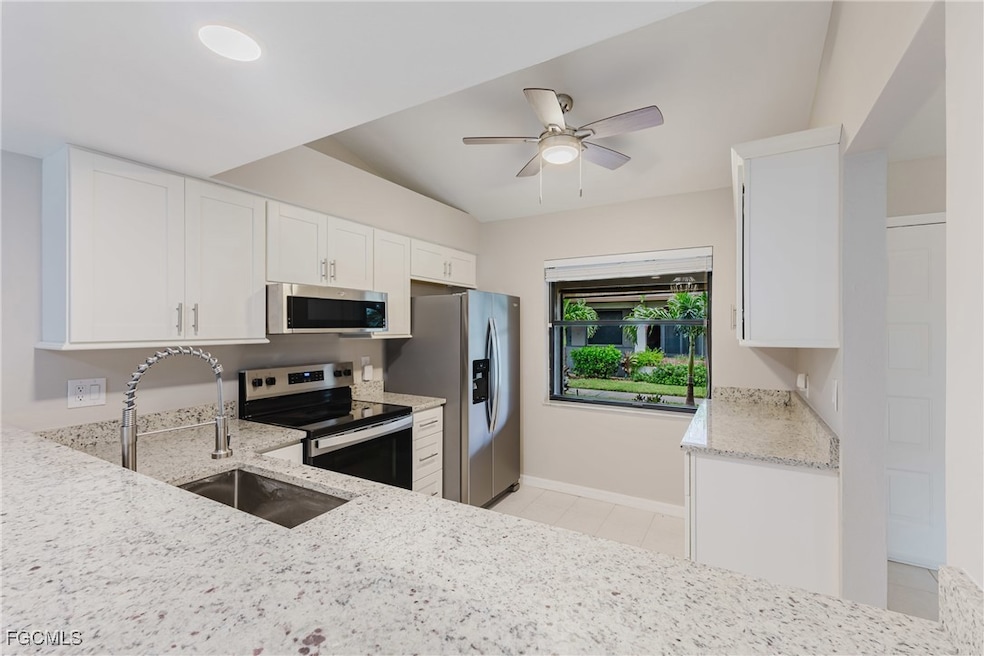Kitchen with white cabinetry, light stone counters, stainless steel appliances, and ceiling fan