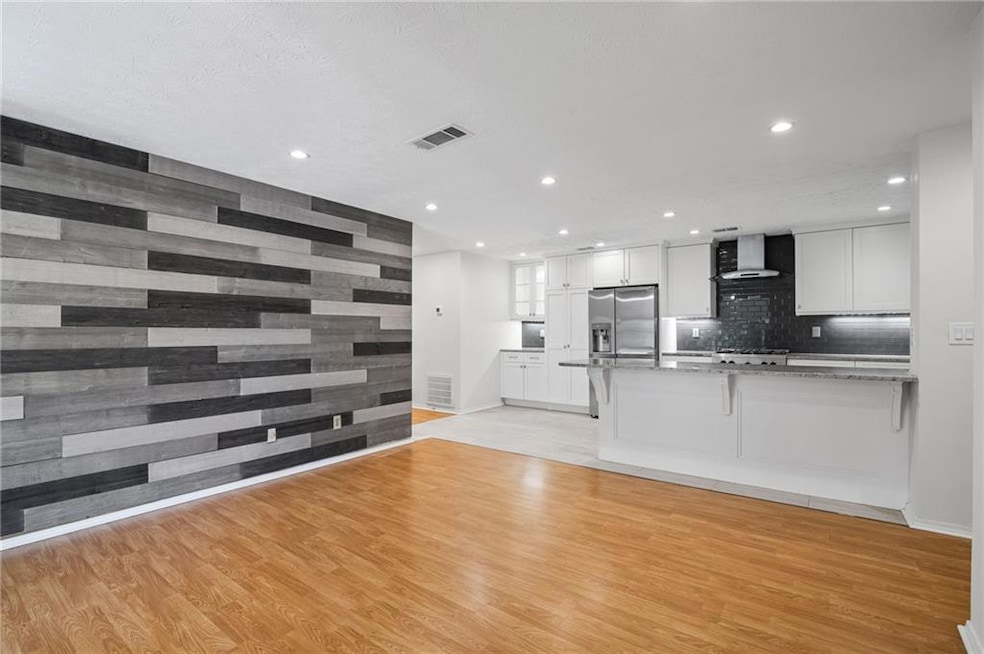 Kitchen with white cabinets, a peninsula, a breakfast bar, light wood-type flooring, and wood walls