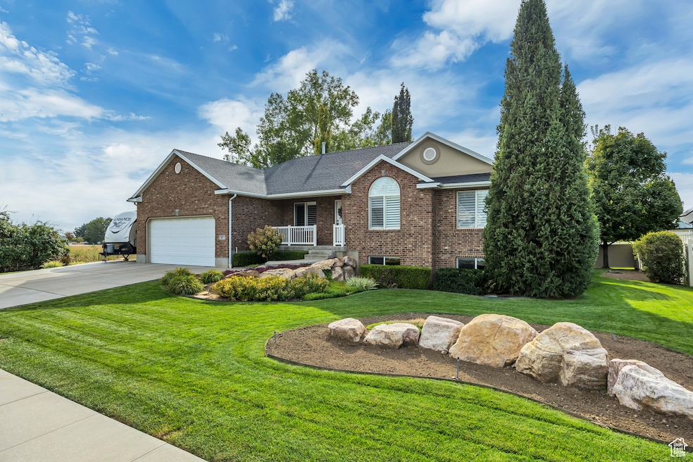 Single story home featuring brick siding, a front yard, driveway, a porch, and a shingled roof