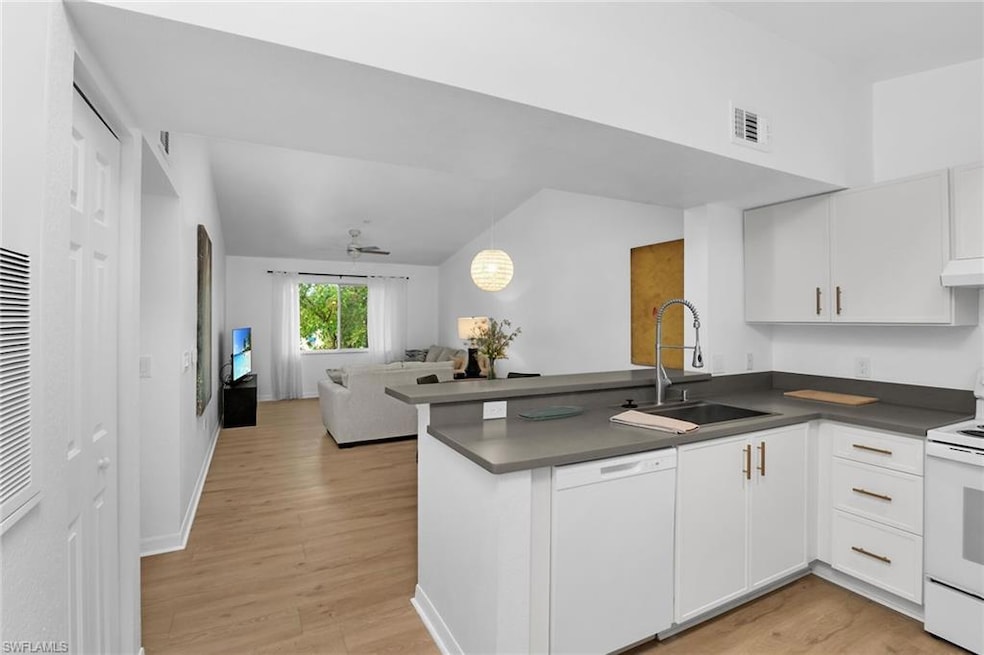 Kitchen with white appliances, a sink, a peninsula, dark countertops, and vaulted ceiling