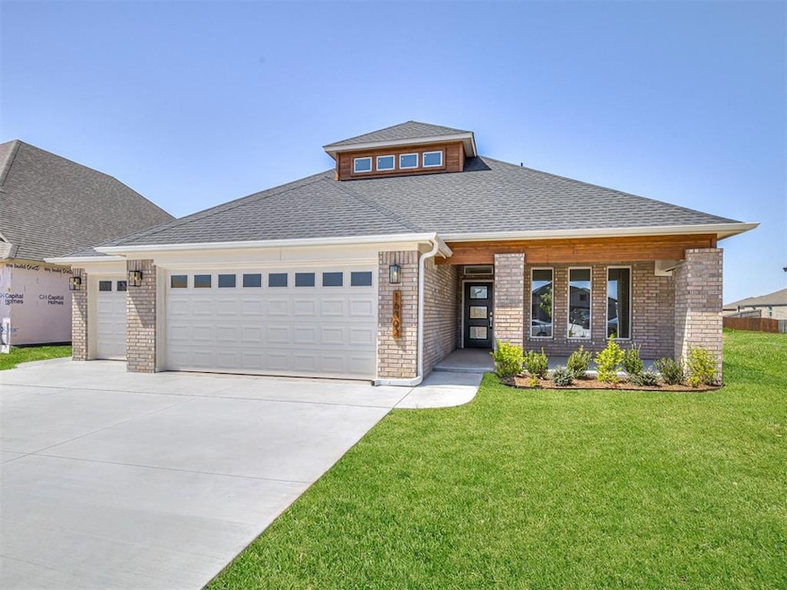 View of front of home featuring brick siding, an attached garage, roof with shingles, a front yard, and driveway