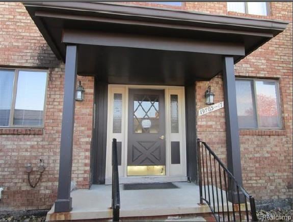View of exterior entry featuring covered porch and brick siding