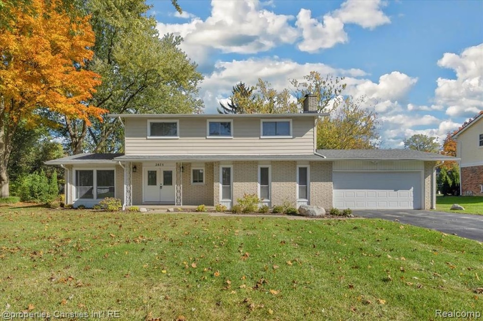 View of front of property with a chimney, brick siding, a front yard, a garage, and a porch