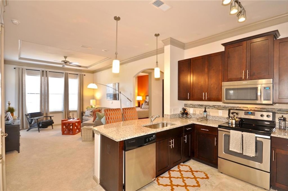 Kitchen with a tray ceiling, hanging light fixtures, stainless steel appliances, ornamental molding, and kitchen peninsula