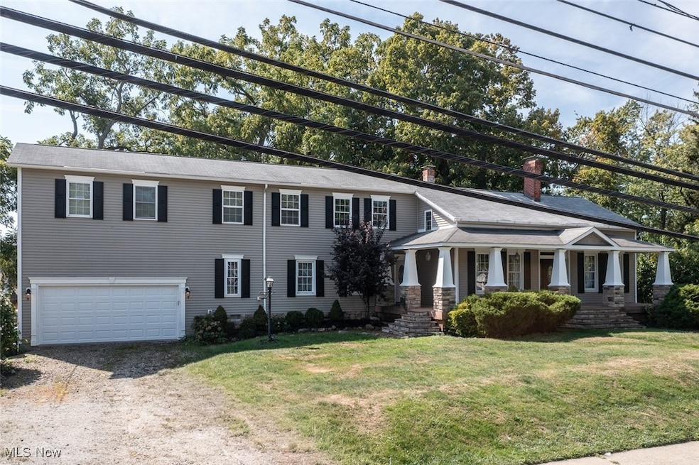 View of front of house with driveway, a chimney, covered porch, an attached garage, and a front yard