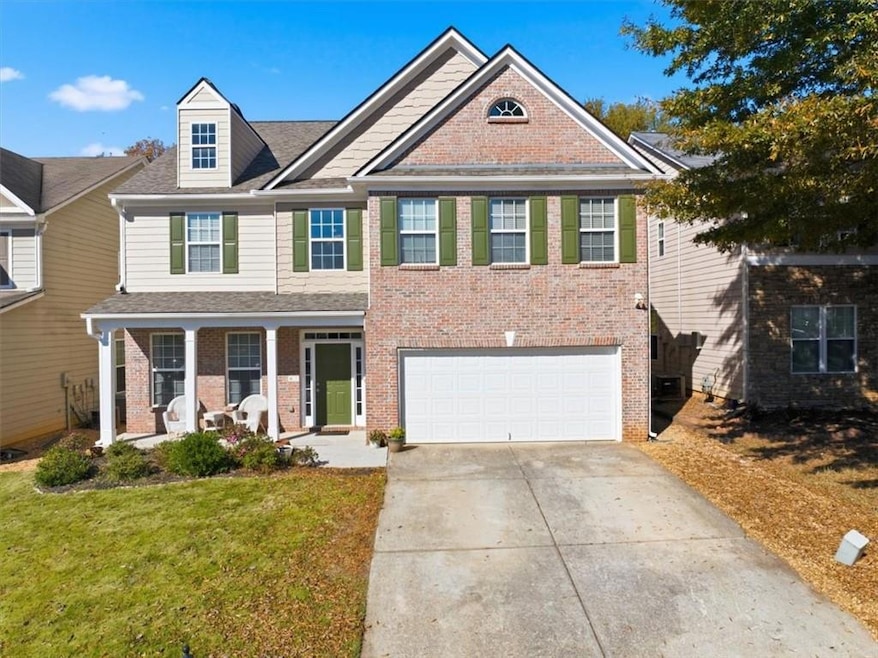 View of front of property featuring a porch, driveway, a garage, brick siding, and a front yard
