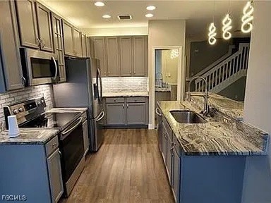 Kitchen featuring appliances with stainless steel finishes, dark stone countertops, dark wood finished floors, decorative backsplash, and recessed lighting
