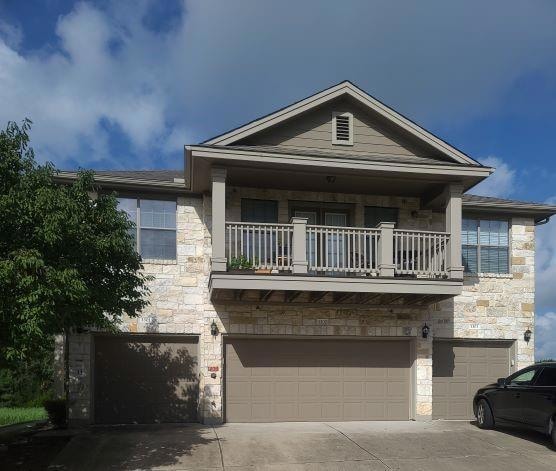 View of front of home with a balcony, stone siding, driveway, and an attached garage